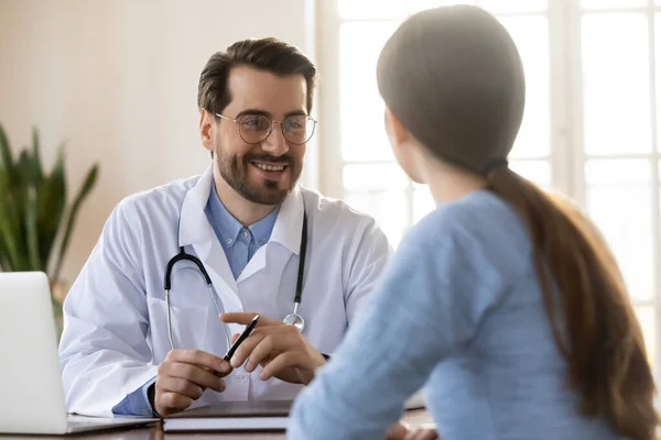 Lächelnder junger Arzt hört sich bei Treffen Patientenbeschwerden an — Stockfoto