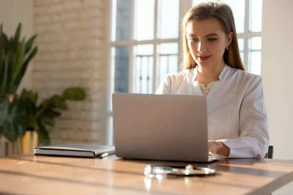 Сосредоточенная молодая женщина врач работает на ноутбуке онлайн в офисе — стоковое фото