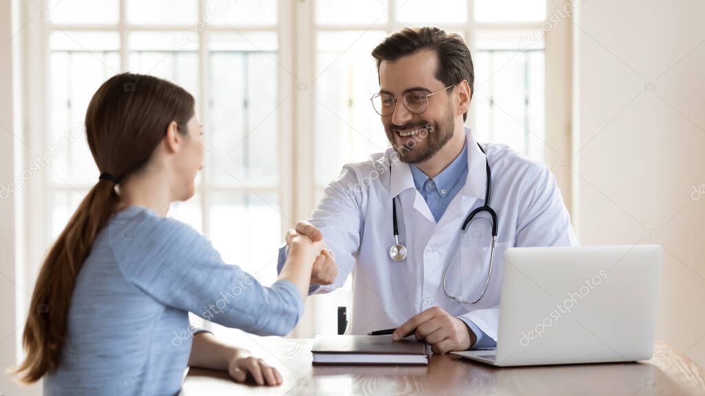 Smiling young doctor wearing uniform shaking female patient hand