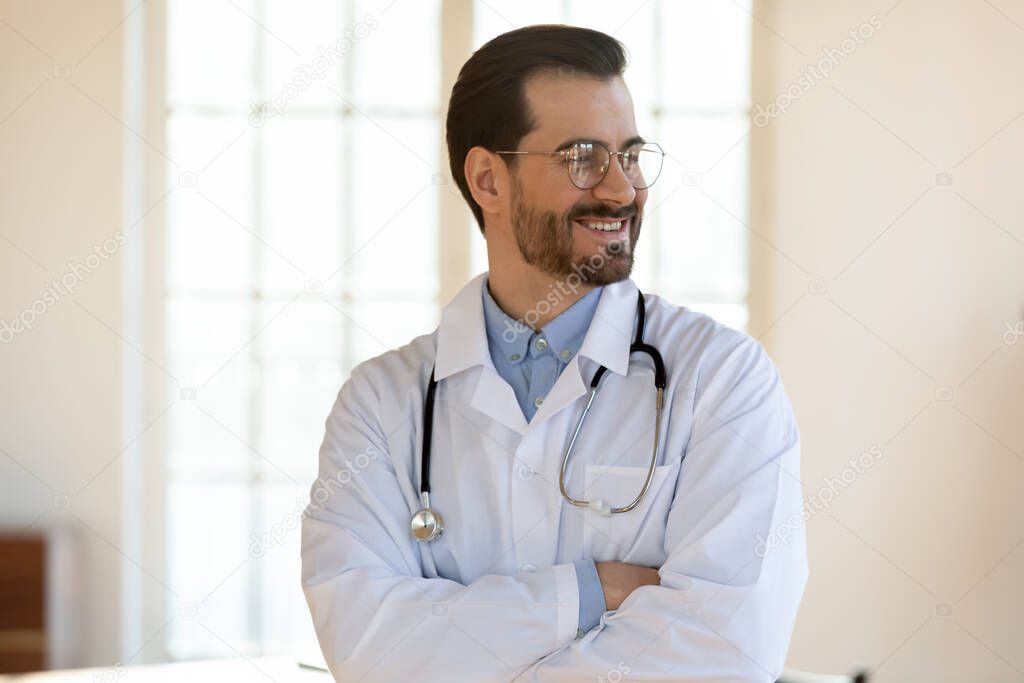 Smiling dreamy young man doctor wearing glasses looking to aside
