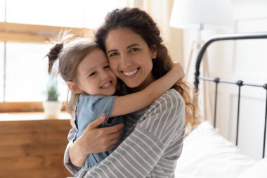 Portre mutlu anne küçük kızı kucaklıyor kameraya bakıyor.