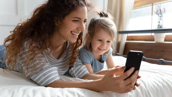 Ξαπλωμένη στο κρεβάτι μητέρα και κόρη χρησιμοποιώντας smartphone κάνοντας videocall — Φωτογραφία Αρχείου