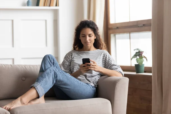 Mulher relaxar no sofá segurando smartphone enviar sms para amigo — Fotografia de Stock