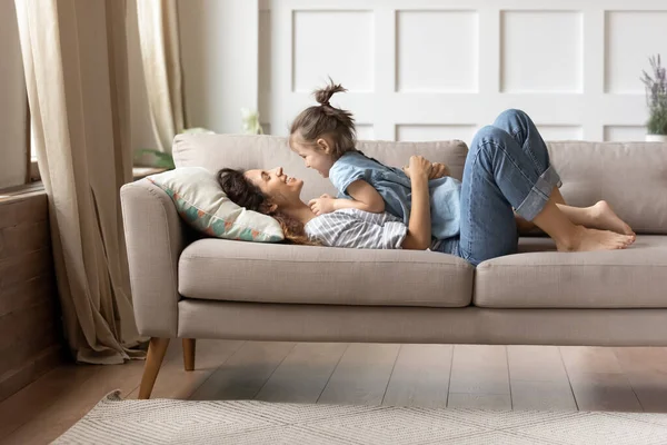 En el sofá acostado feliz madre y su alegre hijita — Foto de Stock