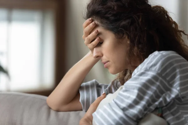 Woman sitting on sofa covers face with palm feels upset — Stock Photo, Image