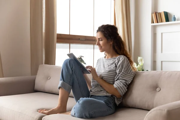 Woman sitting on couch use tablet device chat with friend