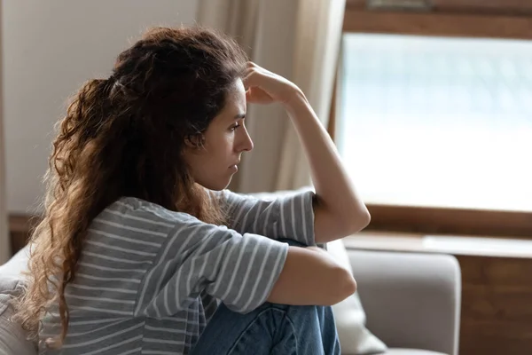 Smutná mladá žena sedí na gauči cítí depresivní boční pohled — Stock fotografie