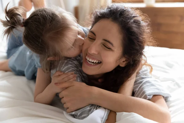Daughter kisses mother cheek lying together in bed feels happy — Stock Photo, Image