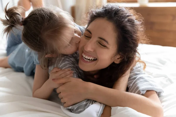 Figlia baci madre guancia sdraiato insieme a letto si sente felice — Foto Stock