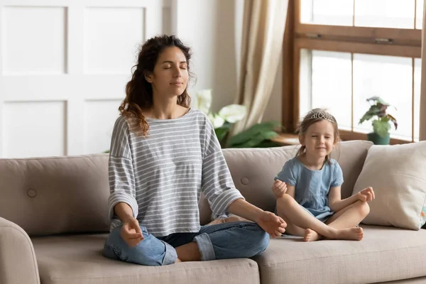 Mother her little daughter meditating sit cross-legged on couch — Stock Photo, Image