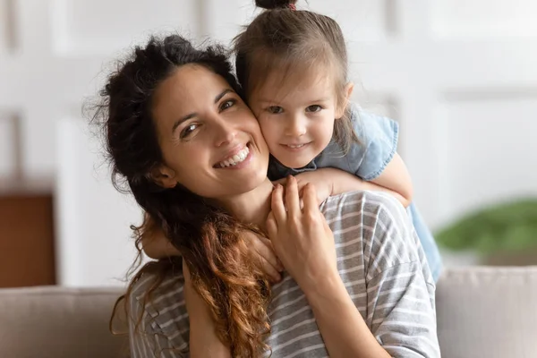 Adorável filha abraços mãe por trás sorrindo olhando para a câmera — Fotografia de Stock