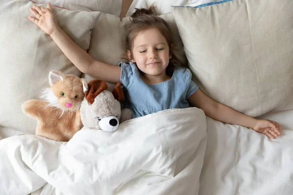 Gadis kecil tidur di tempat tidur dengan mainan binatang berbulu — Stok Foto