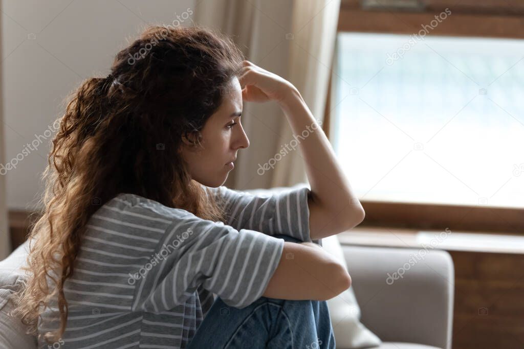 Sad young woman sitting on couch feels depressed side view