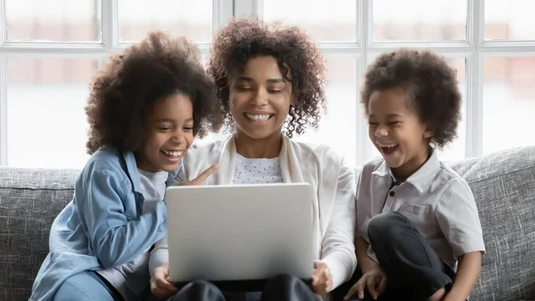 Mutlu genç Afrikalı kadın çocuklarla bilgisayar başında film izliyor..