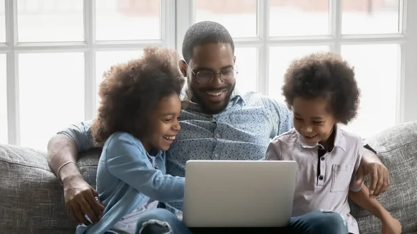 Glad afrikansk amerikansk far använder dator med barn. — Stockfoto
