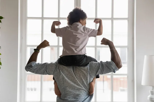 Afro-Amerikaanse vader met kleine zoon op schouders tonen biceps. — Stockfoto