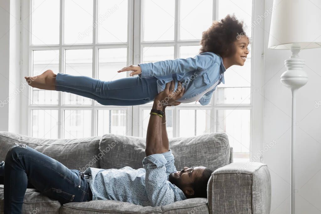 Happy small african ethnicity girl flying on straight daddys arms.