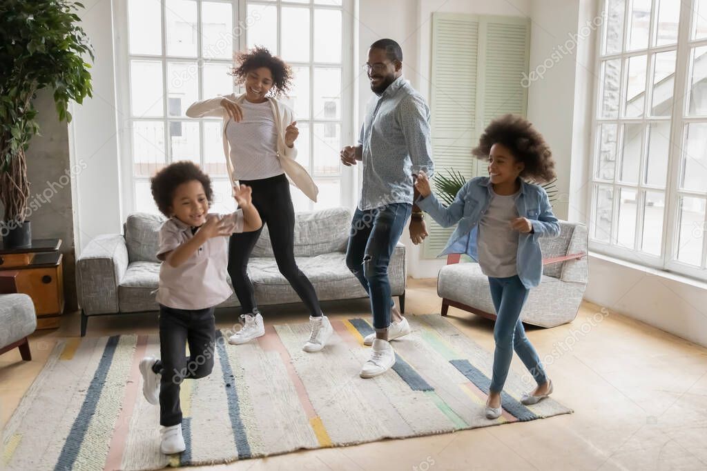 Happy mixed race young parents dancing to music with children.