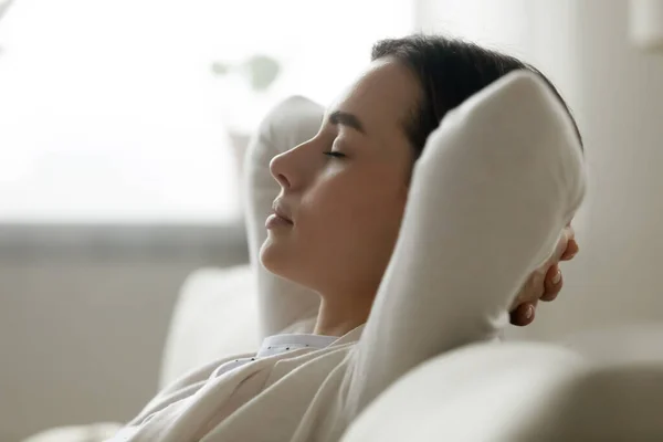 Calm peaceful young beautiful woman daydreaming on sofa.