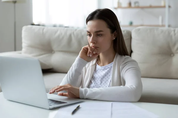 Confused unhappy young woman looking at computer screen.