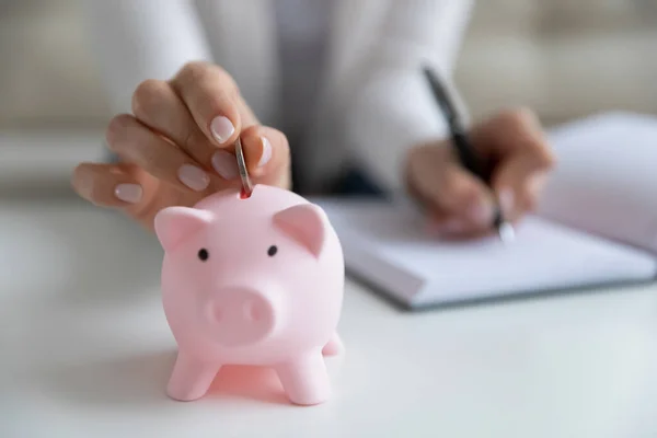 Close up young female hands putting coin in piggybank. — Stock Photo, Image