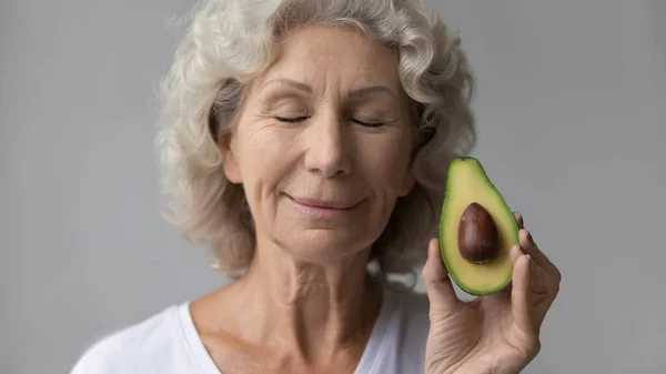 Head shot satisfied mature woman with closed eyes holding avocado