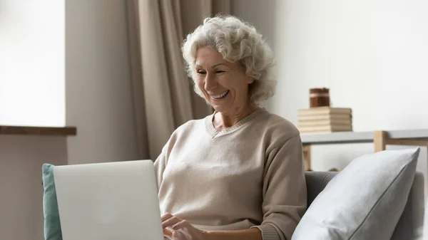 Улыбающаяся женщина средних лет смотрит на экран ноутбука дома — стоковое фото