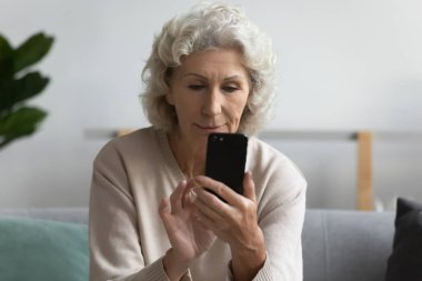 Ciddi bir orta yaşlı kadın akıllı telefon kullanıyor, ekrana bakıyor.