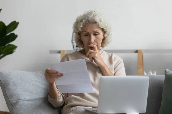 Προσεκτική ώριμη γυναίκα ανάγνωση επιστολή, χρησιμοποιώντας το laptop, που εργάζονται με αλληλογραφία — Φωτογραφία Αρχείου