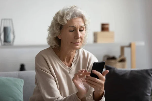 Окаменелая зрелая женщина, пользующаяся телефоном дома, глядя на экран — стоковое фото