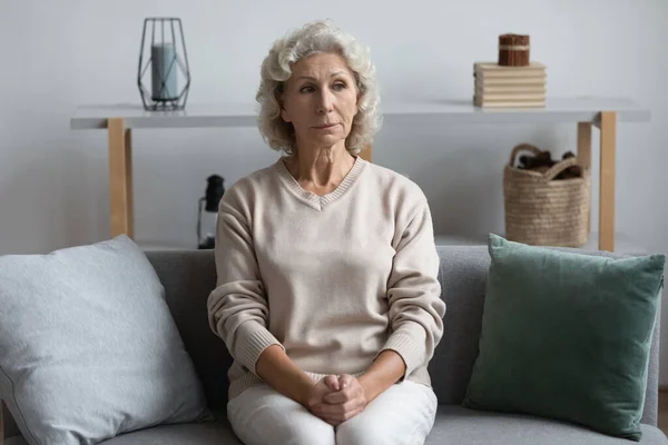 Thoughtful mature woman lost in thoughts, sitting on couch alone — Stock Photo, Image