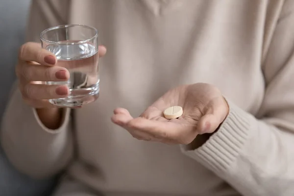 Close up mature woman holding glass of water and pill — Stock Photo, Image