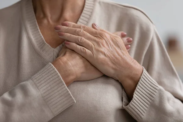 Sluiten up hoopvolle dankbare volwassen vrouw houden handen op de borst — Stockfoto