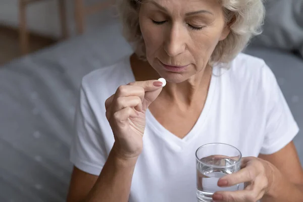 Close up mature woman holding pill and glass of water — Stock Photo, Image