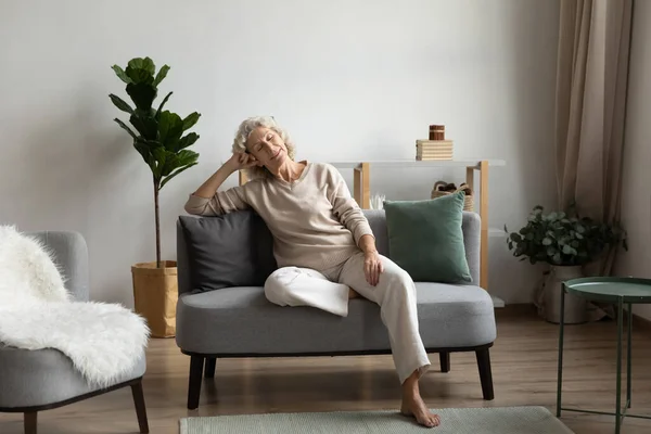 Calm mature woman sitting, relaxing on cozy couch at home