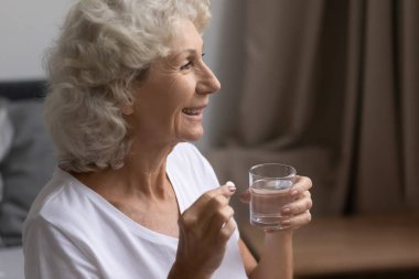 Gülümseyen olgun bir kadın ilaç alıyor, yuvarlak haplar tutuyor.