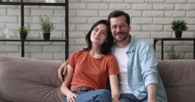 Birbirine aşık bir çift kanepeye oturmuş kameraya bakıyor.