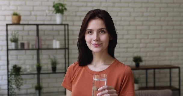 Женщина улыбается, глядя в камеру, держа стакан с тихой водой — стоковое видео