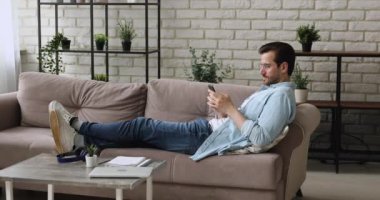 Kanepeye yaslanan adam akıllı telefondan mesaj atıyor.