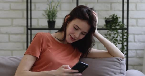 25-річна жінка розслабляється на дивані вдома за допомогою мобільного телефону — стокове відео