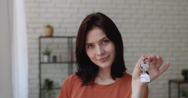 En lykkelig ung kvinne som står innendørs med nøkler fra nye leiligheter – stockvideo