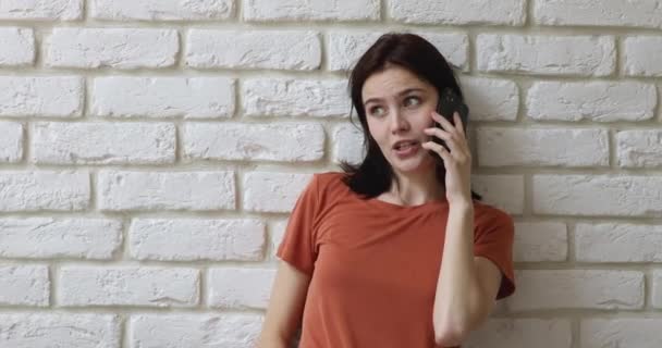 Mujer apoyada en la pared de ladrillo sosteniendo teléfono inteligente hablando con un amigo — Vídeos de Stock