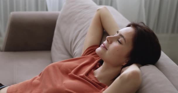 Женщина кладет руки за голову расслабляясь опираясь на диван — стоковое видео