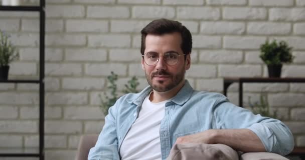 Hombre con gafas sonriendo mirando a la cámara sentarse en el sofá — Vídeos de Stock