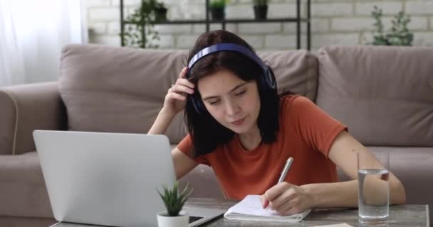 Chica escribiendo en copybook escuchar audio a través de auriculares navegar por Internet — Vídeos de Stock