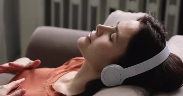 Las mujeres usan auriculares descansando en el sofá escuchar música — Vídeos de Stock