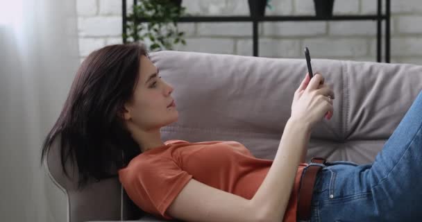リラックスした女の子うそ上のソファとともにスマートフォン — ストック動画