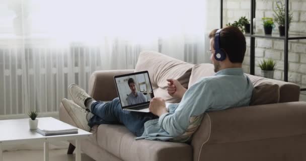 Man met koptelefoon in gesprek met vriend met behulp van videoconferentie en laptop — Stockvideo