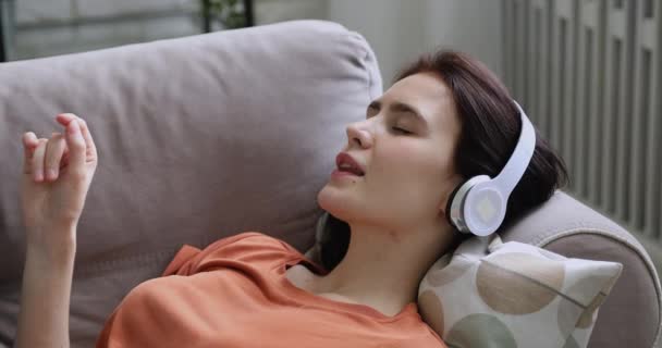 Menina usar fones de ouvido deitado relaxante no sofá desfrutar de música clássica — Vídeo de Stock