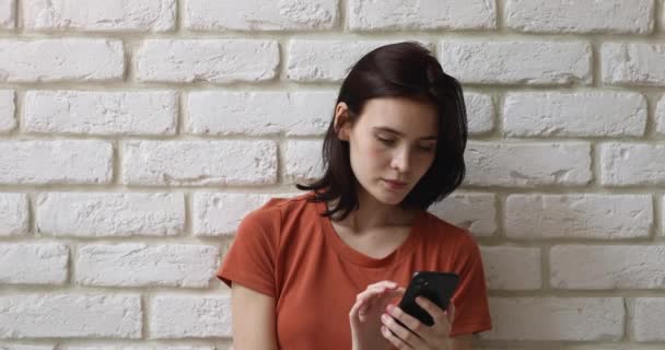 Κορίτσι που χρησιμοποιεί smartphone στέκεται ενάντια σε λευκό φόντο τοίχο τούβλο — Αρχείο Βίντεο